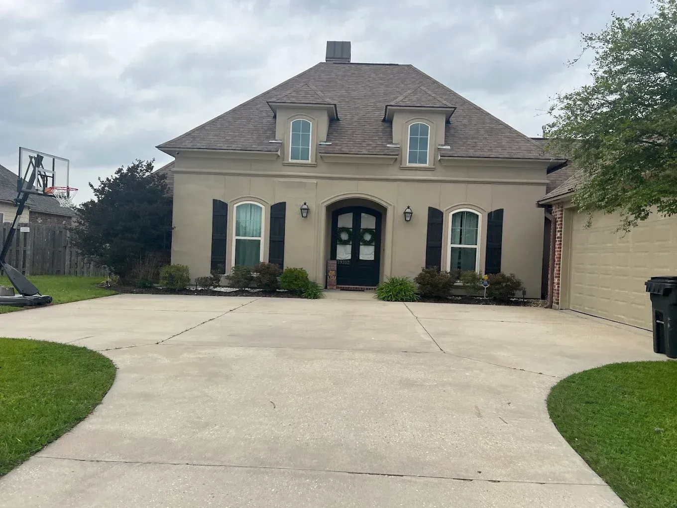 Beige house with black shutters, arched front door, and driveway.