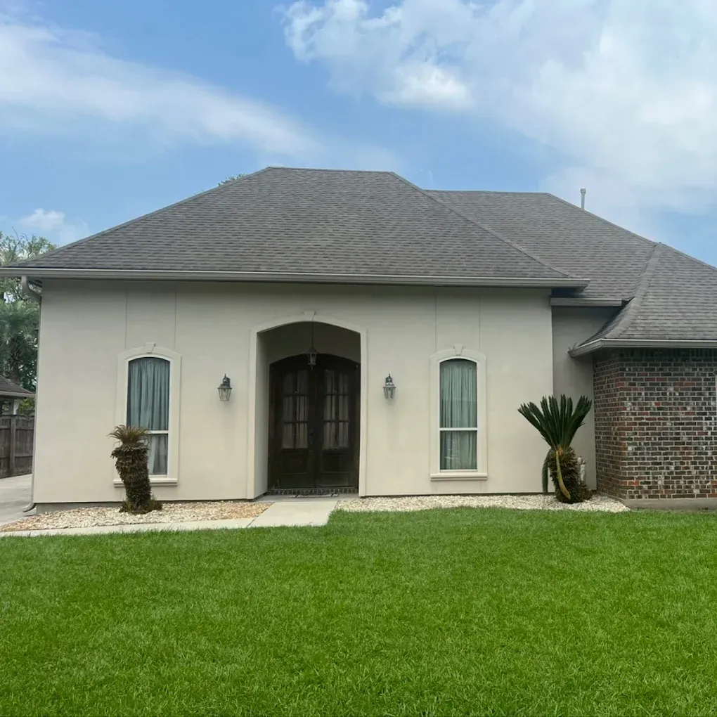 Beige stucco home with brown roof, double doors, and palm trees in front yard.