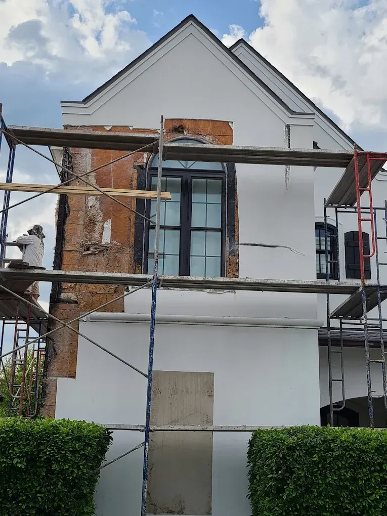 House under renovation; scaffolding, exposed brick, white walls, and a person working on the left side.