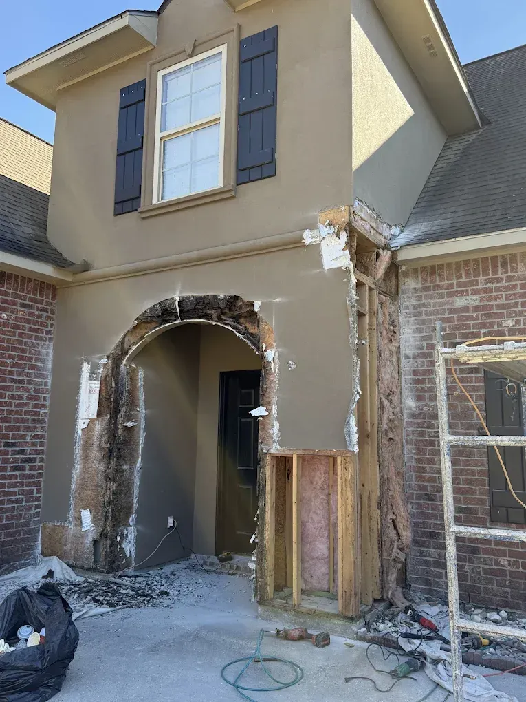 House entrance undergoing repair; damaged stucco exposes wood framing and door.