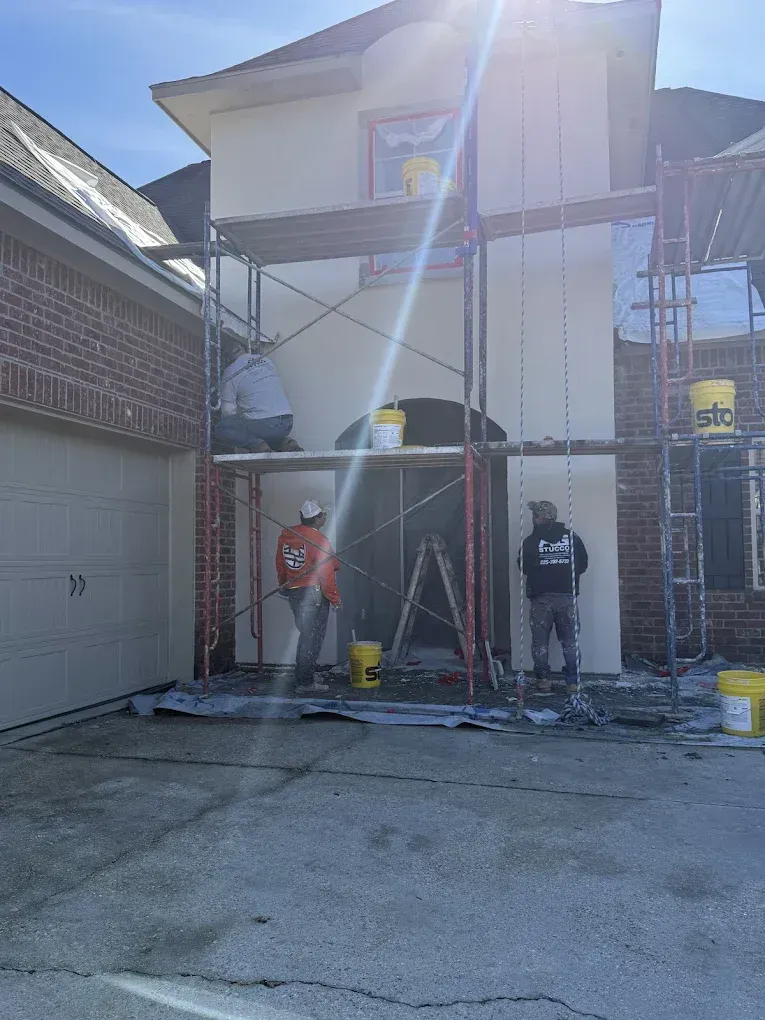 Construction workers on scaffolding, applying stucco to a building's exterior.