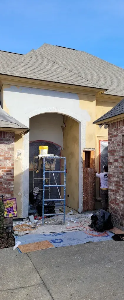 Exterior construction site, doorway being renovated with scaffolding, brick and concrete. Person working. Debris on ground.