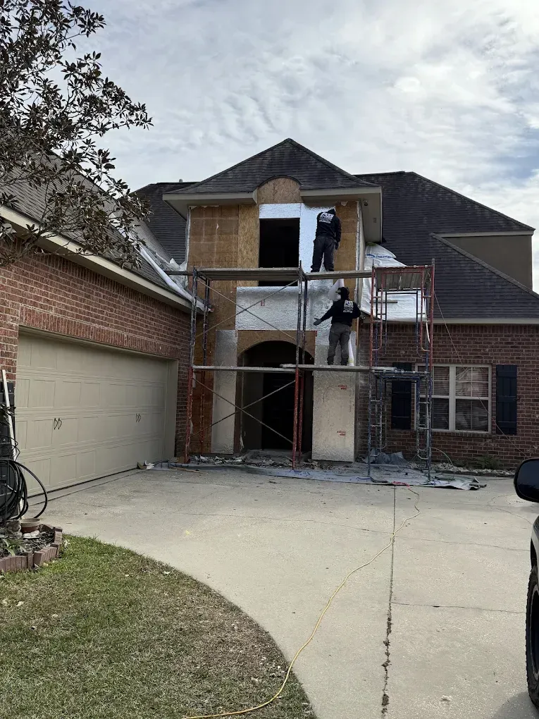 Construction workers on scaffolding, working on a two-story house exterior.