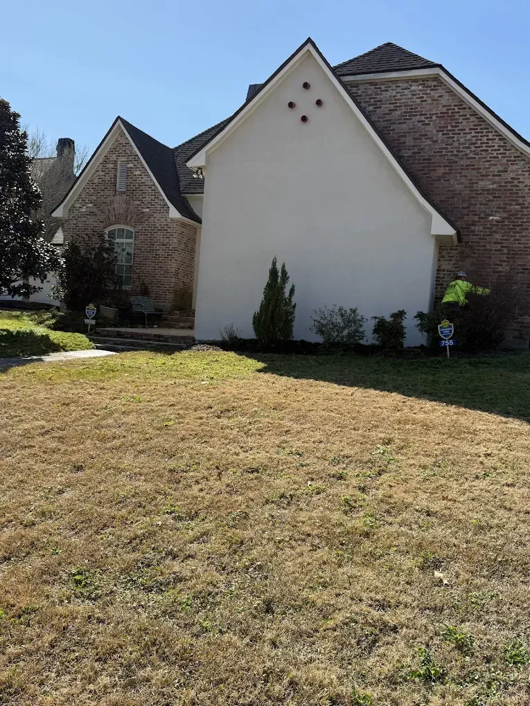House with a brick exterior, white siding, and brown roof on a sunny day.