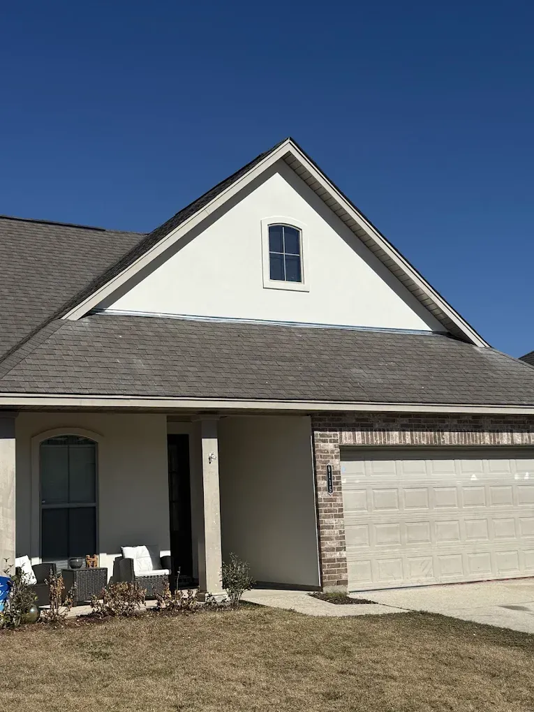 Tan house with a garage, front door, and a small window under a gabled roof against a blue sky.