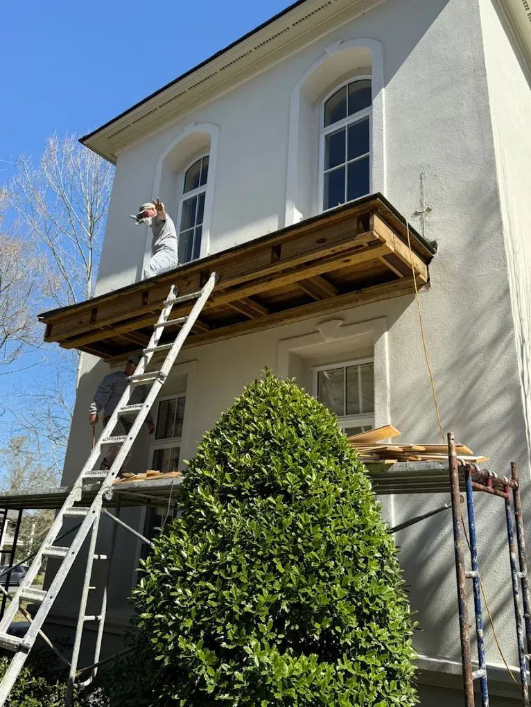 Construction workers on a ladder and platform repairing a two-story white building.