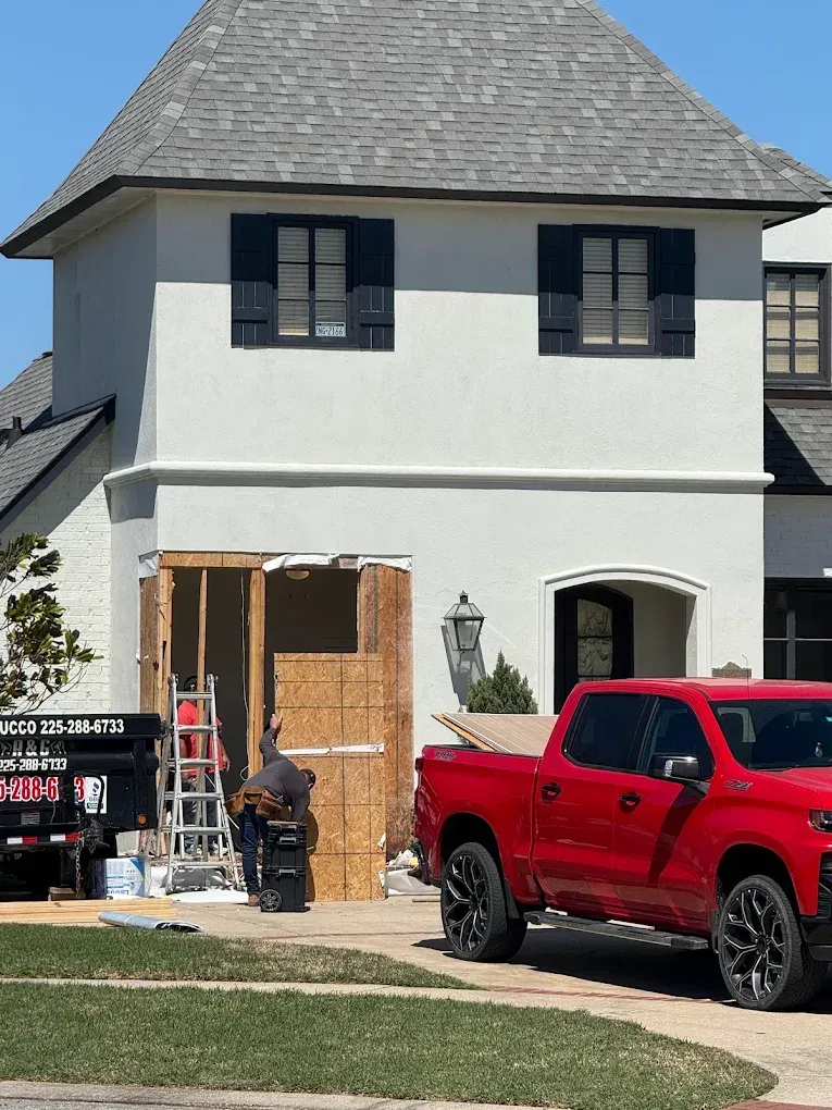 Construction in progress on a white house with a red truck and a work truck in the driveway.