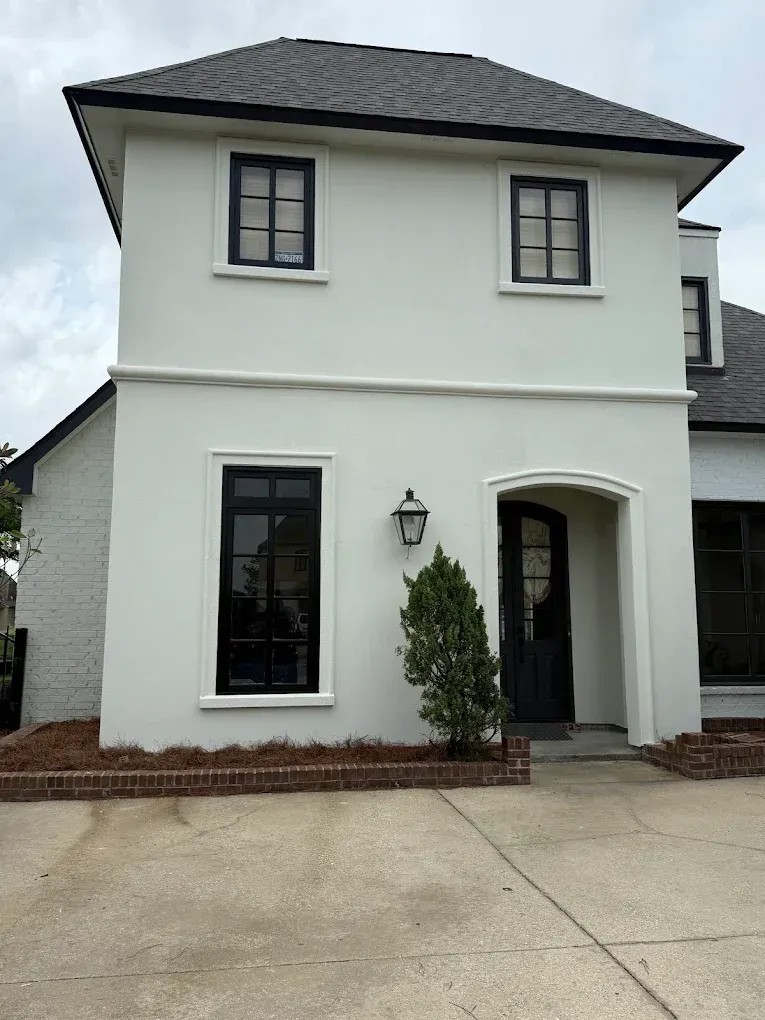 White stucco house with black trim and windows, arched doorway.