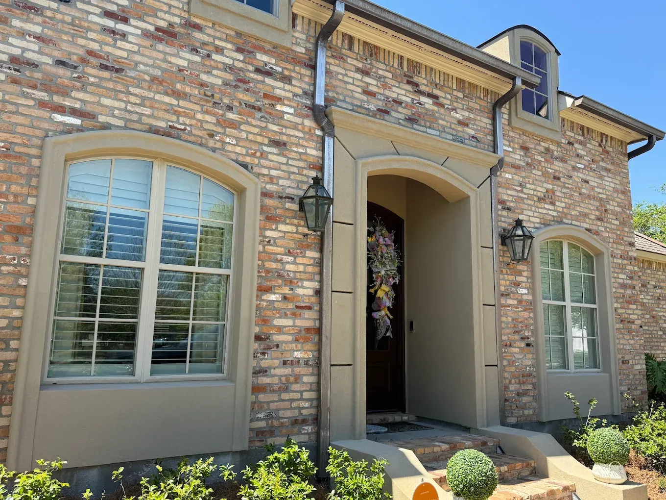 Brick house with arched windows and doorway, dark shutters, and tan trim.