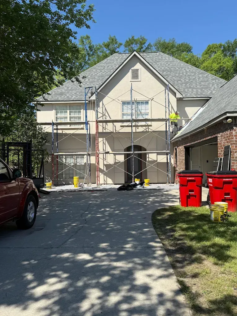 House under construction with scaffolding. Workers painting the stucco exterior. Sunny day.