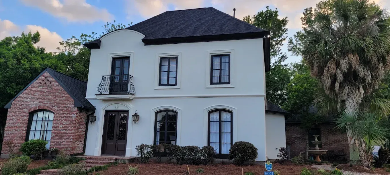 Two-story white house with black roof and trim, brick extension, and black windows.
