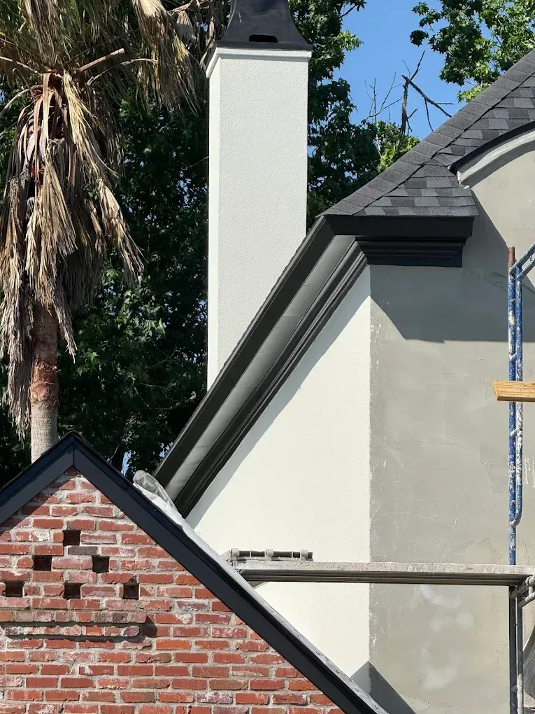 Chimney and building exterior with white stucco, black trim, and a brick section.