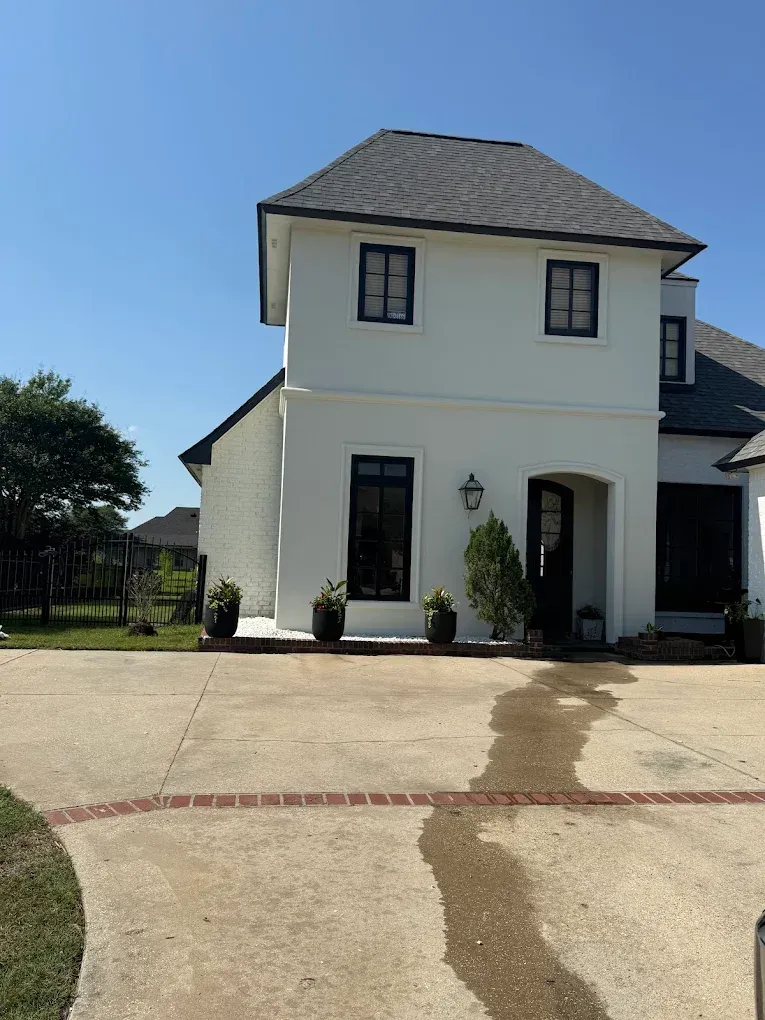 White house with black-framed windows and a dark roof under a blue sky, on a concrete driveway.