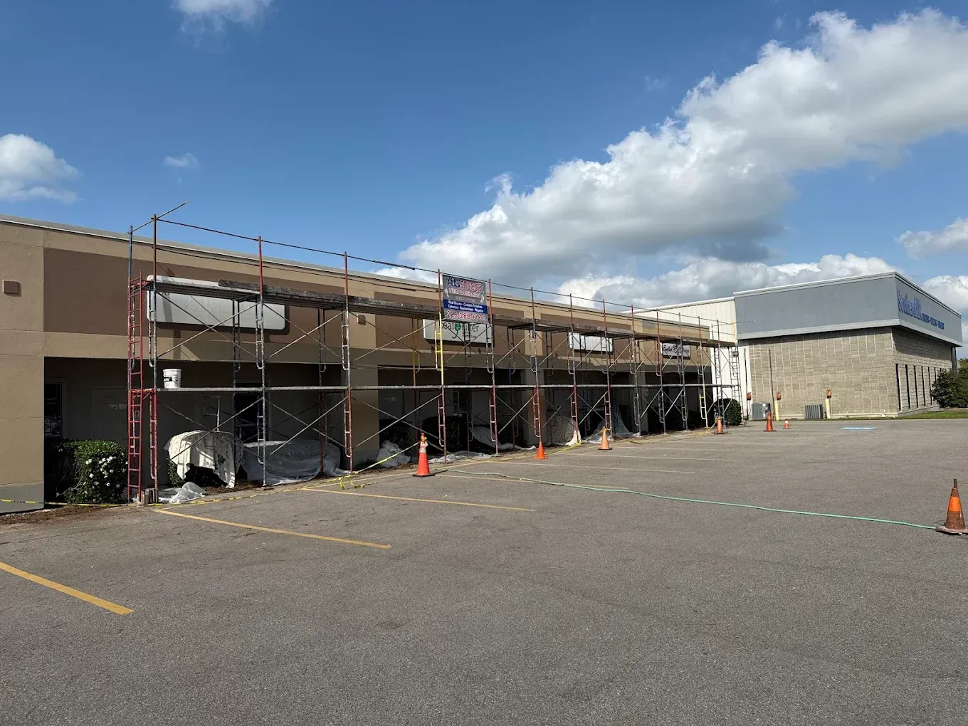 Building exterior under construction with scaffolding and safety cones in a parking lot.
