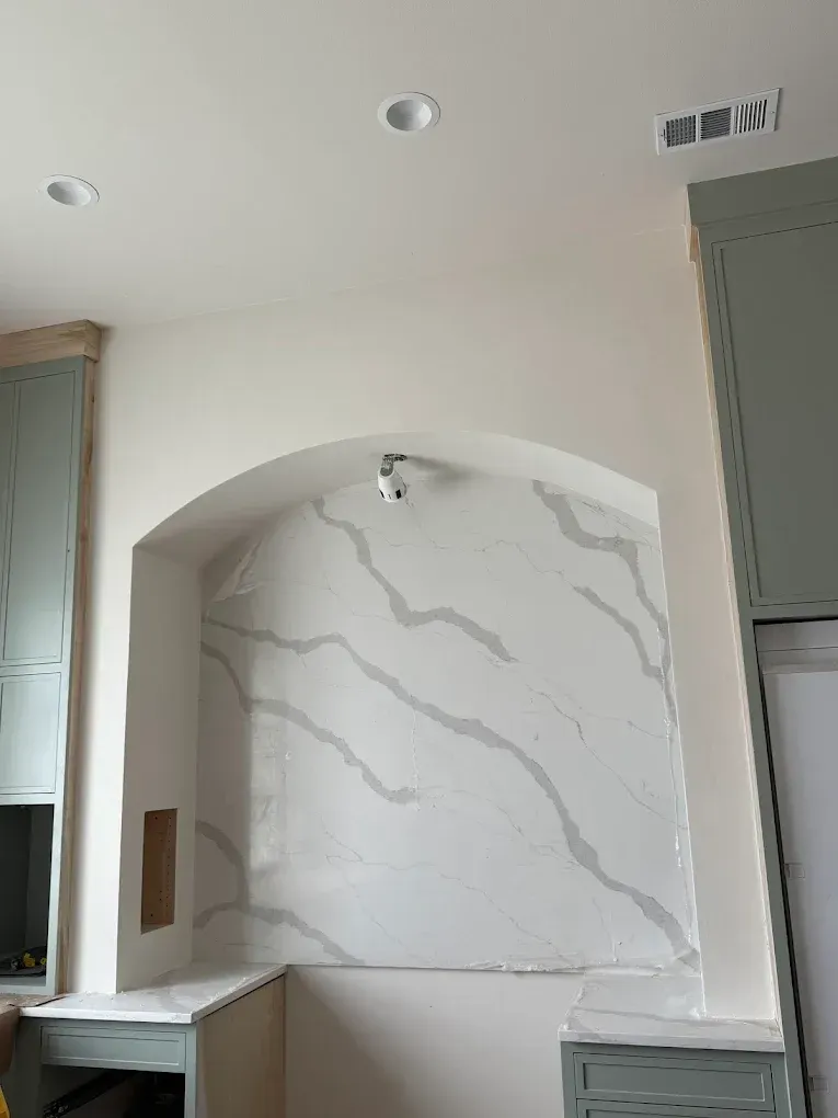 Kitchen niche with white quartz backsplash, light gray veining, arch, recessed lights, and blue-green cabinets.