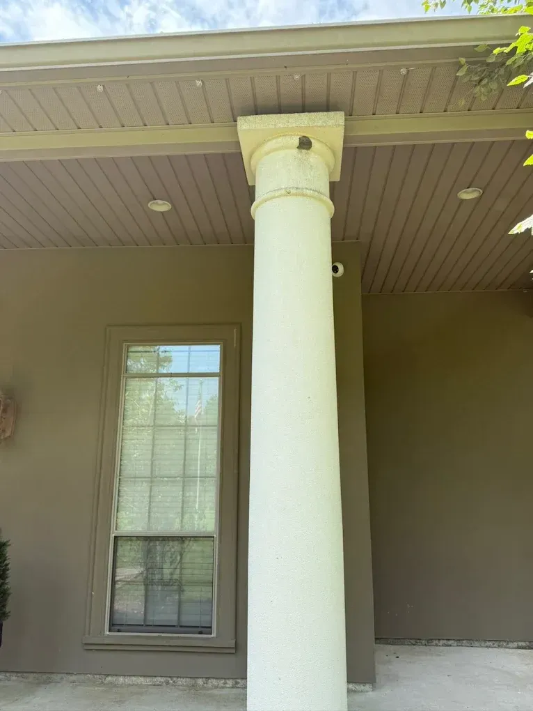 White fluted column supports a brown porch overhang. Window is to the left, against a taupe wall.