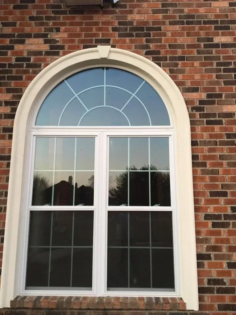 White-framed arched window on a brick building; top pane has arched grid, lower panes have square grid.