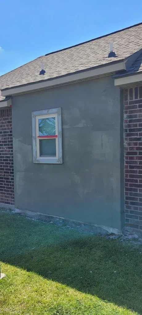 Exterior wall with window, brick and stucco. Green grass and blue sky.
