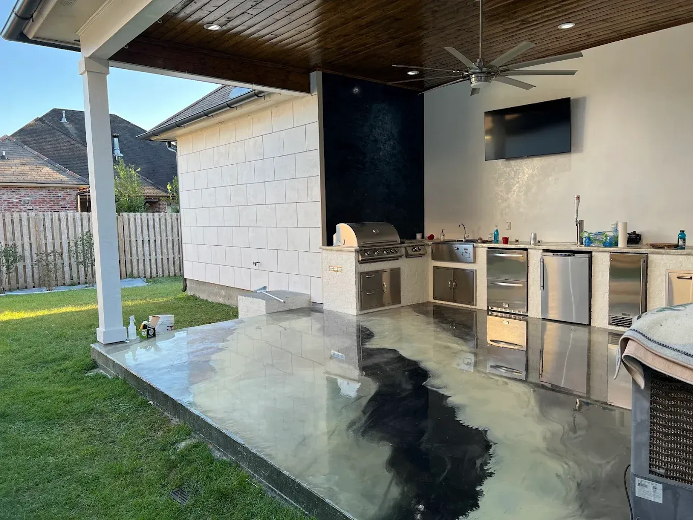 Outdoor kitchen with stainless steel appliances, black accent wall, and metallic floor on a patio.