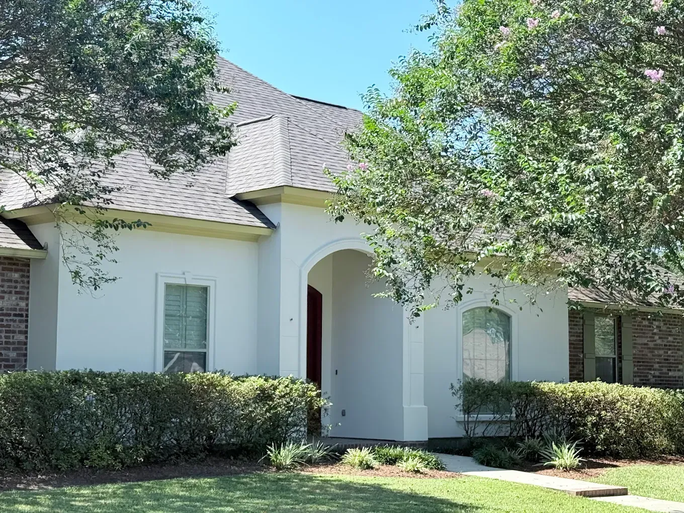 White stucco house with dark roof, arched doorway, and green landscaping.