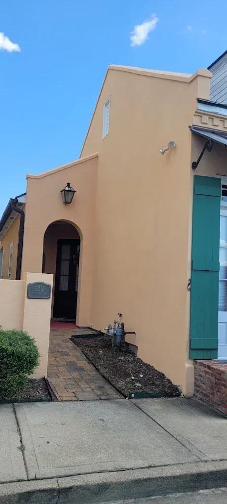 Tan building with green shutters, arched doorway, and a brick pathway.