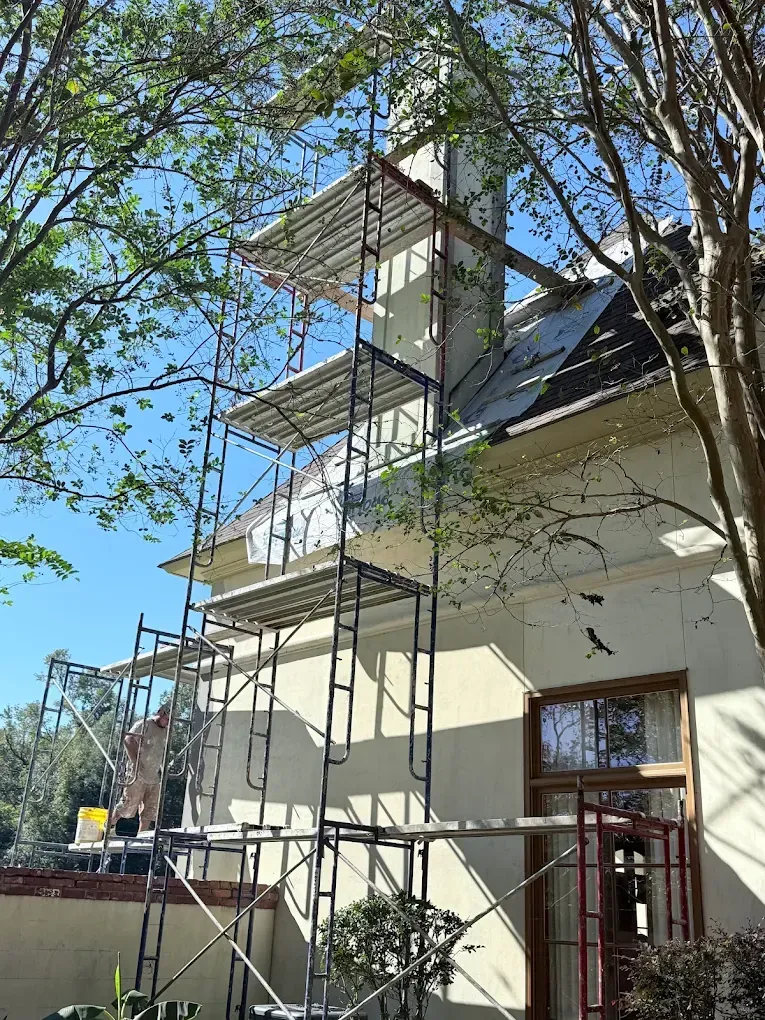 Scaffolding next to a building, a worker is on the platform, and clear blue sky overhead.