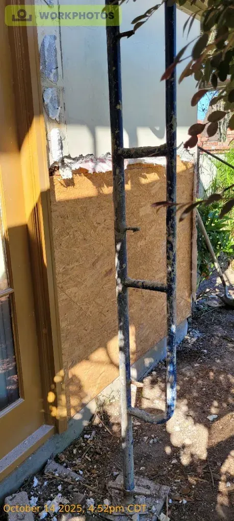 A ladder leans against a building under renovation. OSB board is attached to the exterior wall.