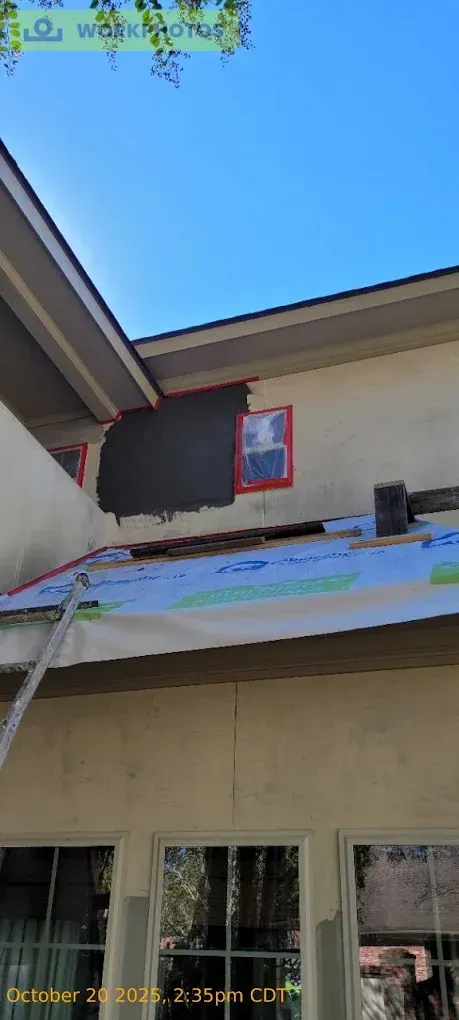 Exterior house painting in progress: a dark gray section, ladder, windows, and clear blue sky.