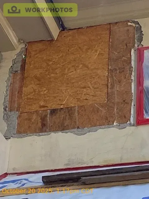Wall with exposed concrete and plywood patching a damaged area.