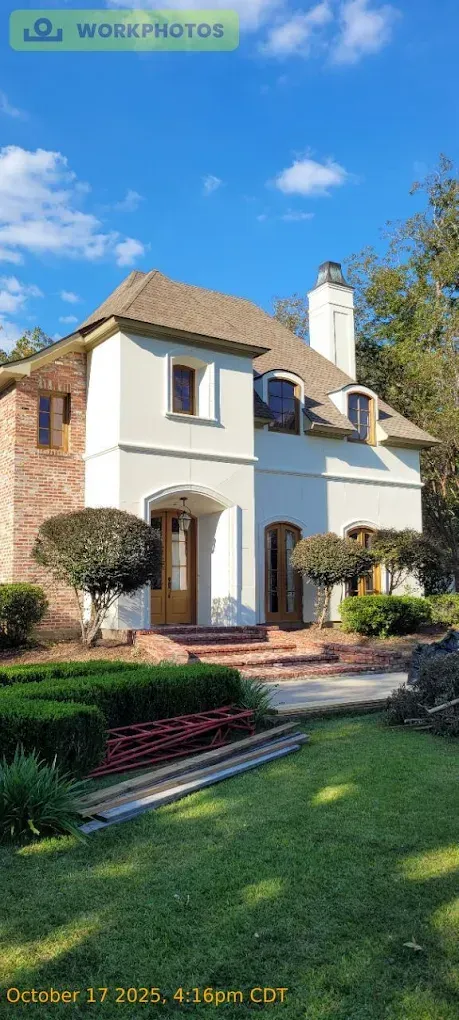 White house with brown roof and brick accents, in front of green lawn and blue sky.