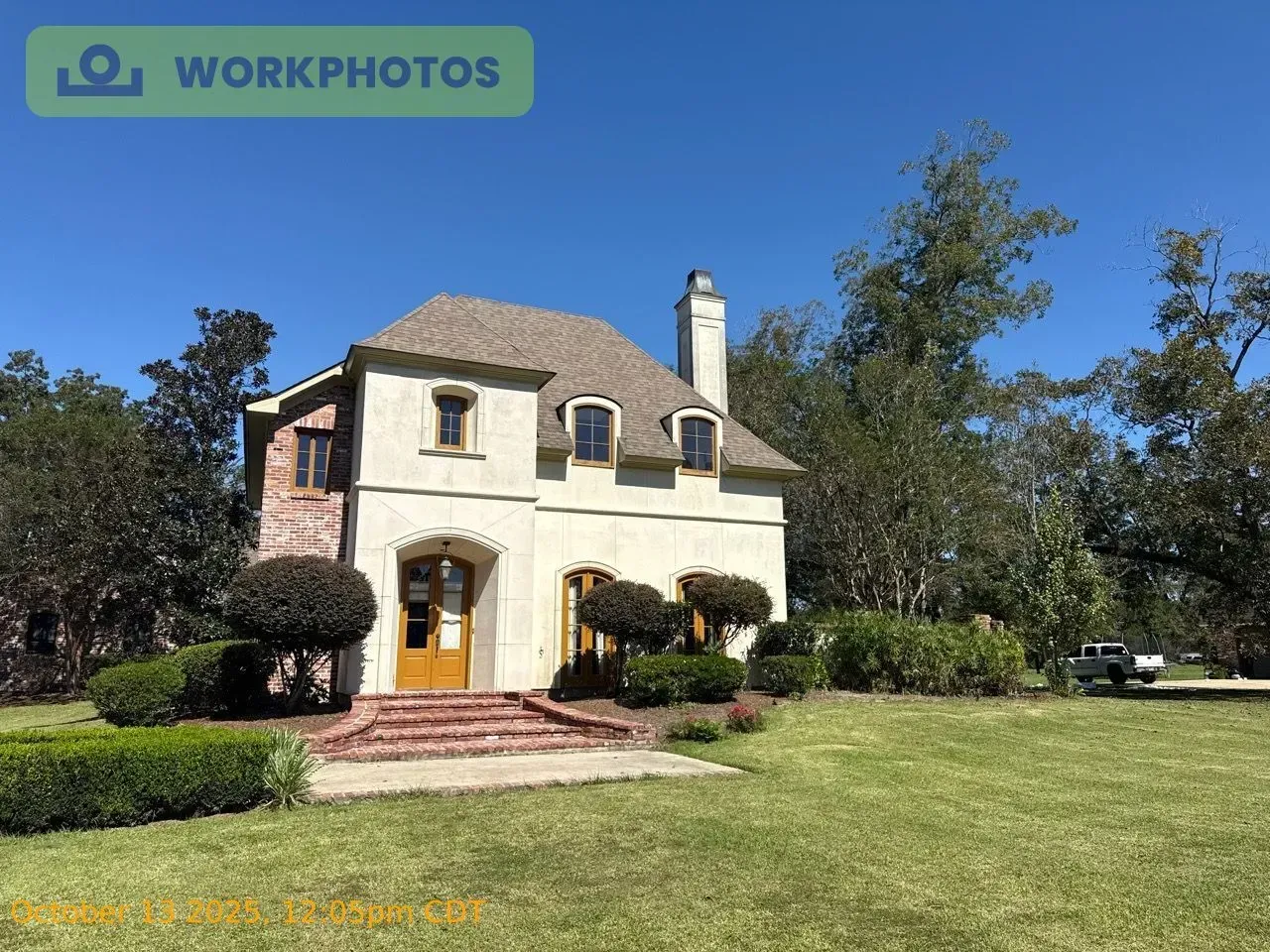 A cream and brick-colored house with a brown roof and a green lawn under a blue sky.
