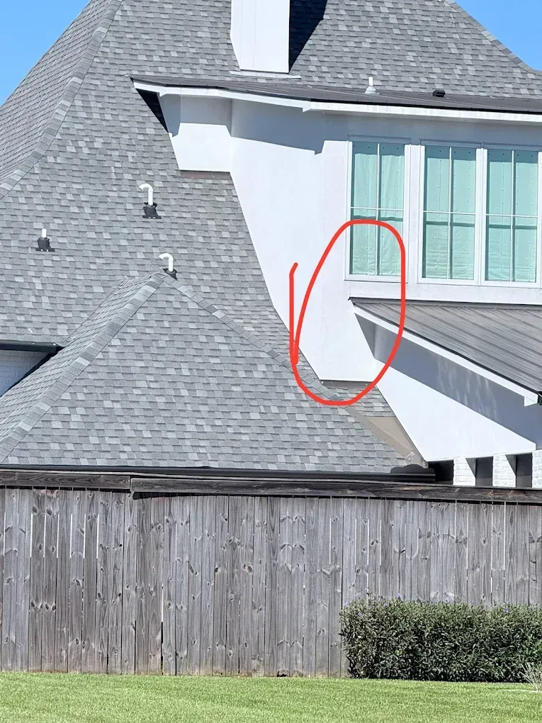 White house corner with gray roof, window, and wooden fence. Red circle highlights wall.