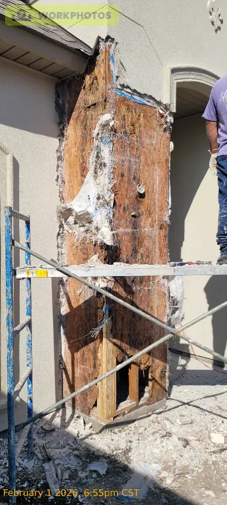 A damaged wooden support column on a building, covered in deteriorated material, and scaffolding present.