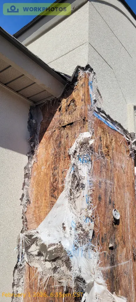 Damaged exterior wall corner showing exposed wood and stucco.