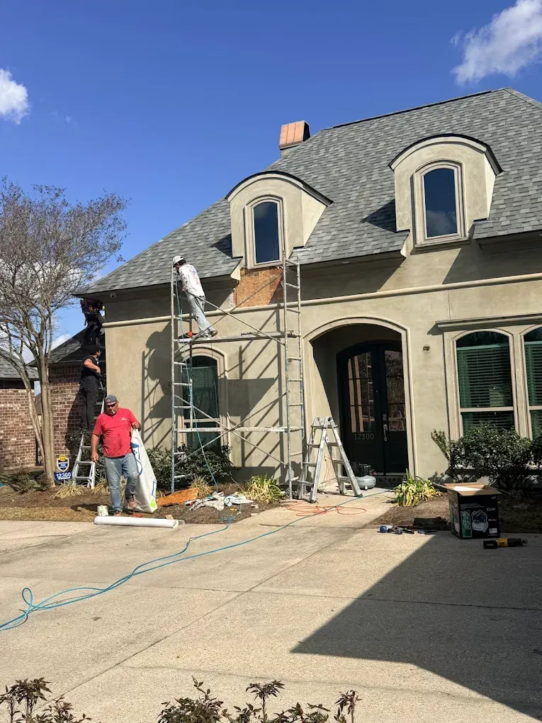 Construction workers on scaffolding repairing the stucco facade of a house.