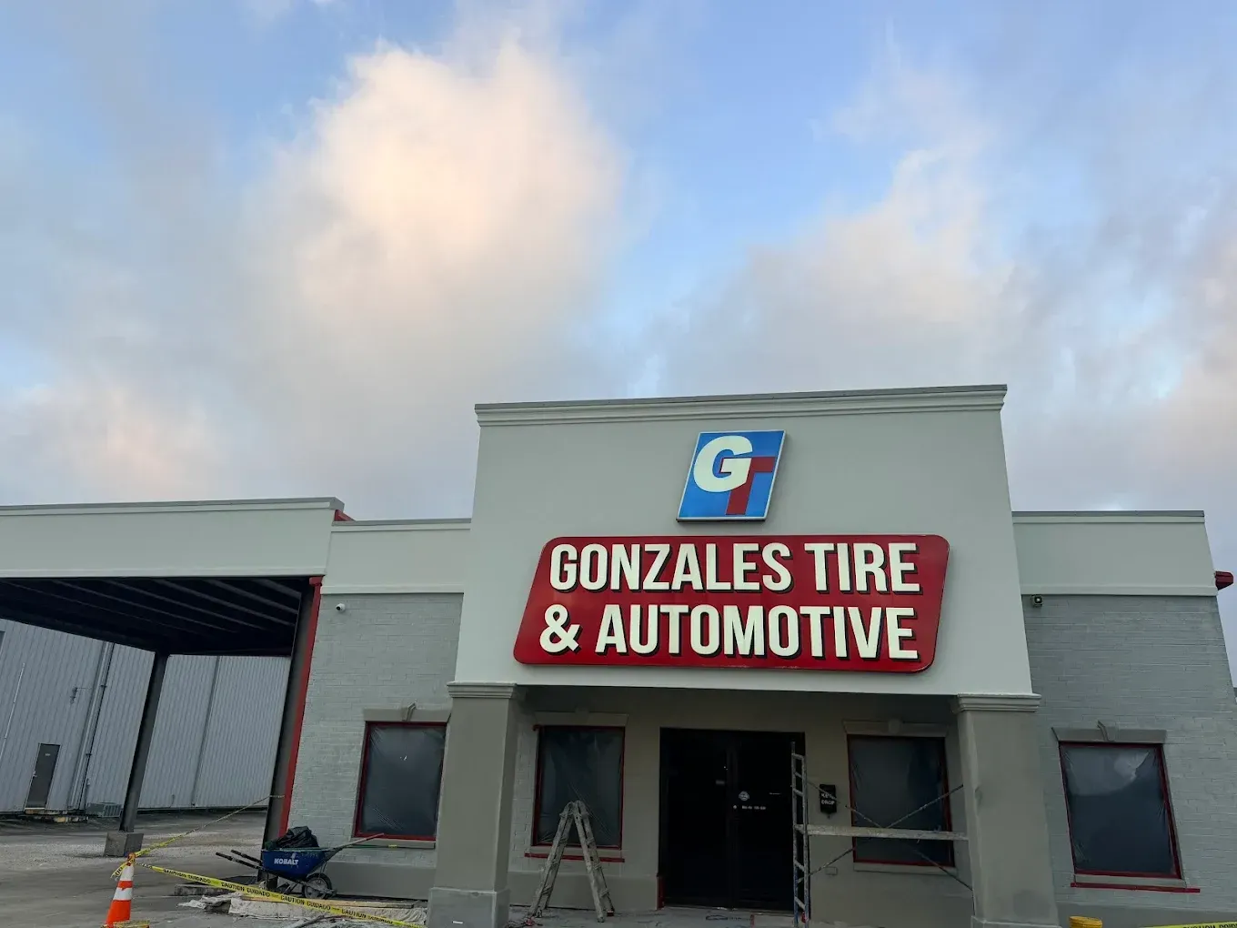 Gonzales Tire & Automotive building with red and blue signage, cloudy sky.