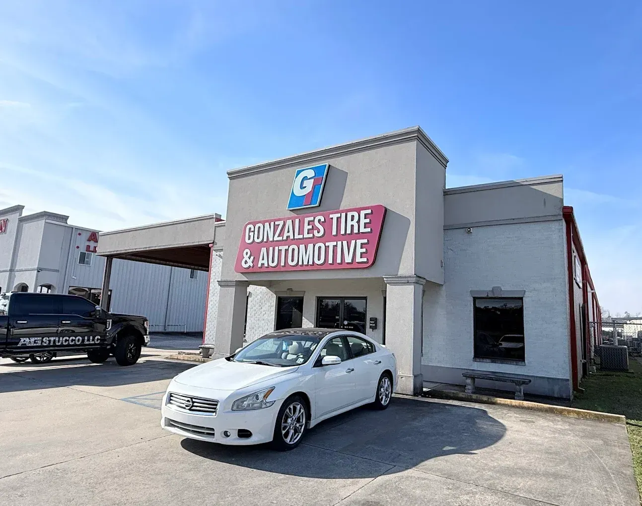 White car parked in front of Gonzalez's Tire & Automotive building. Blue sky.