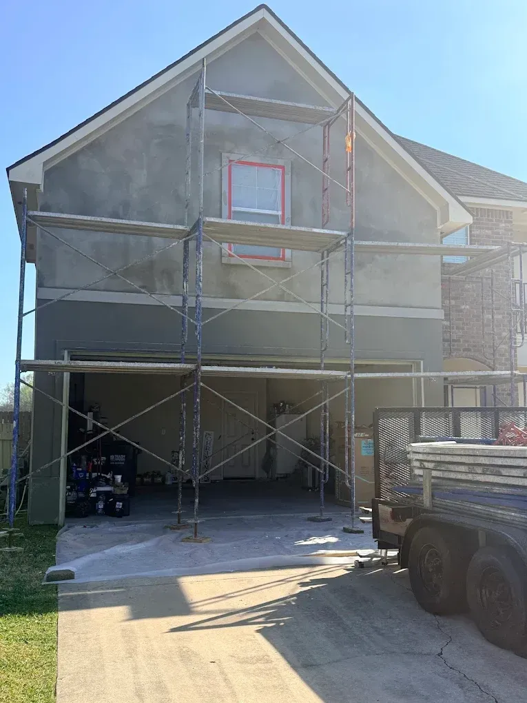 House exterior under stucco repair, scaffolding erected in front of the garage entrance.