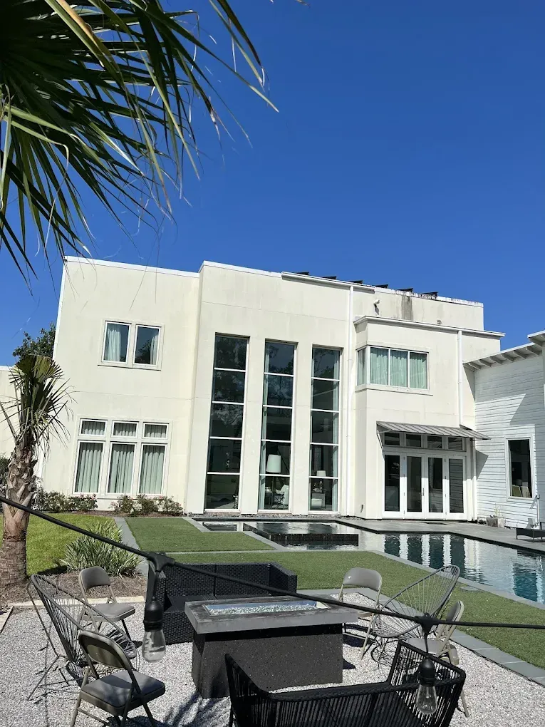 White stucco house with large windows, patio, and pool. Blue sky in background.