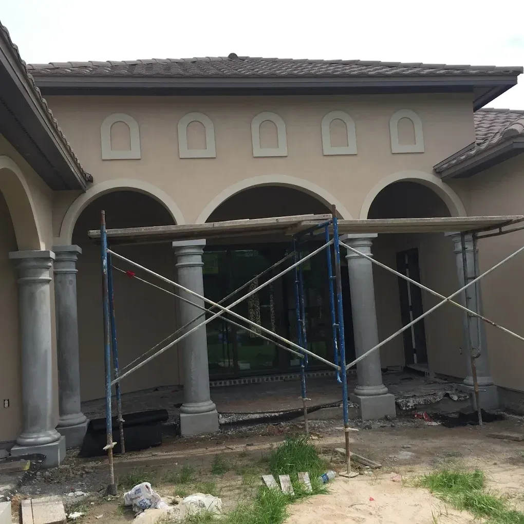 Beige building exterior with arches and columns, under construction with scaffolding.