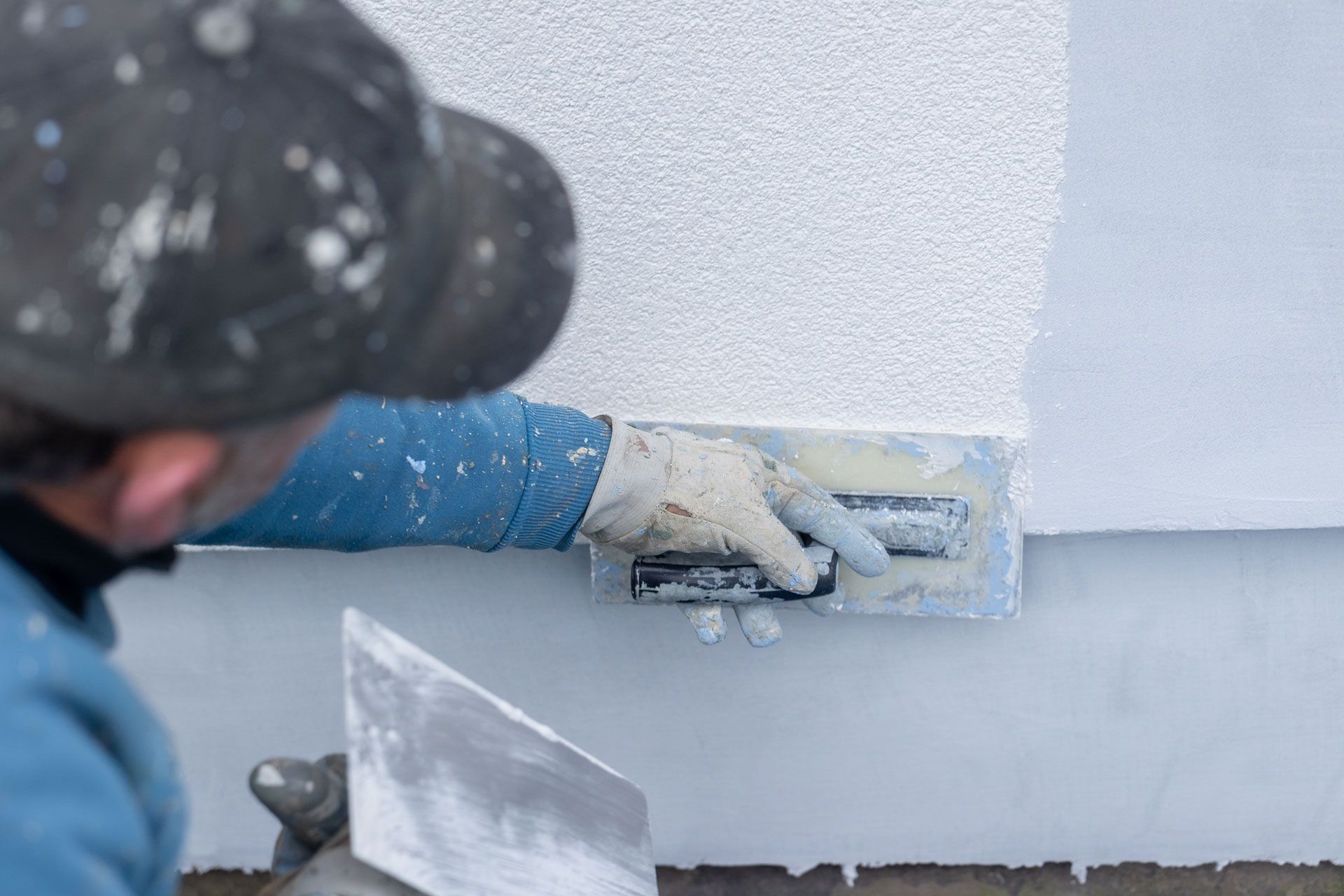 Person applying white stucco to a wall with a trowel outdoors.