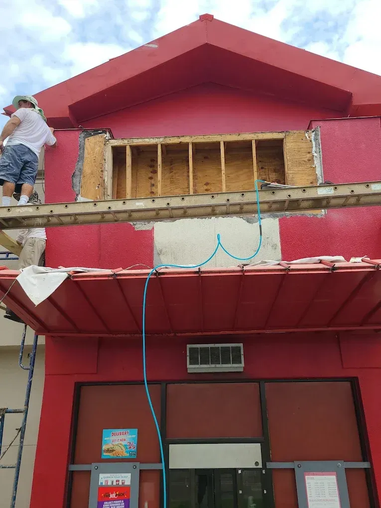 Red building with exposed framework, worker on ladder, construction underway.