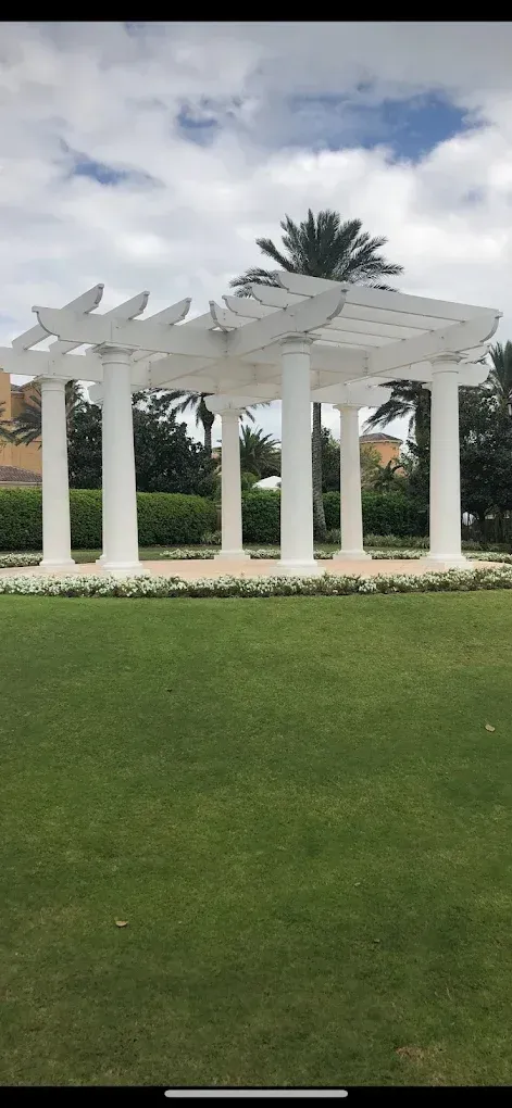 White gazebo with columns on green grass, under a cloudy sky.