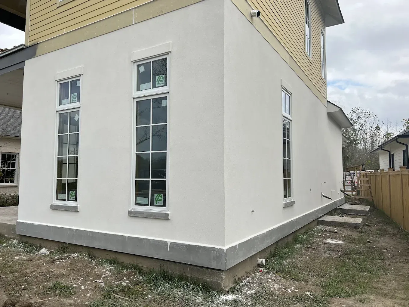 Exterior of a two-story building with white stucco walls, three tall windows, and a gray concrete foundation.