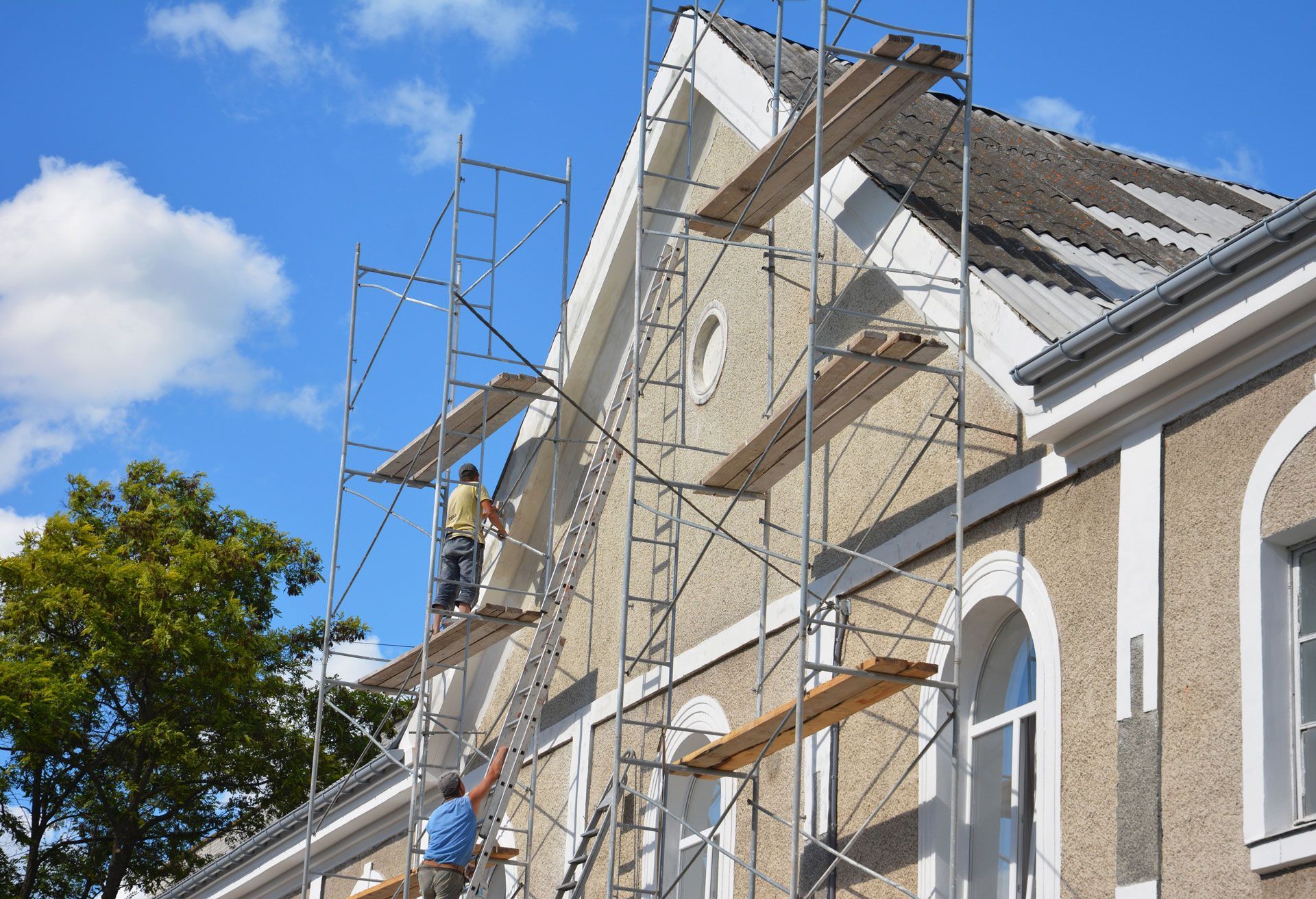 Workers on scaffolding repairing a building's exterior on a sunny day.