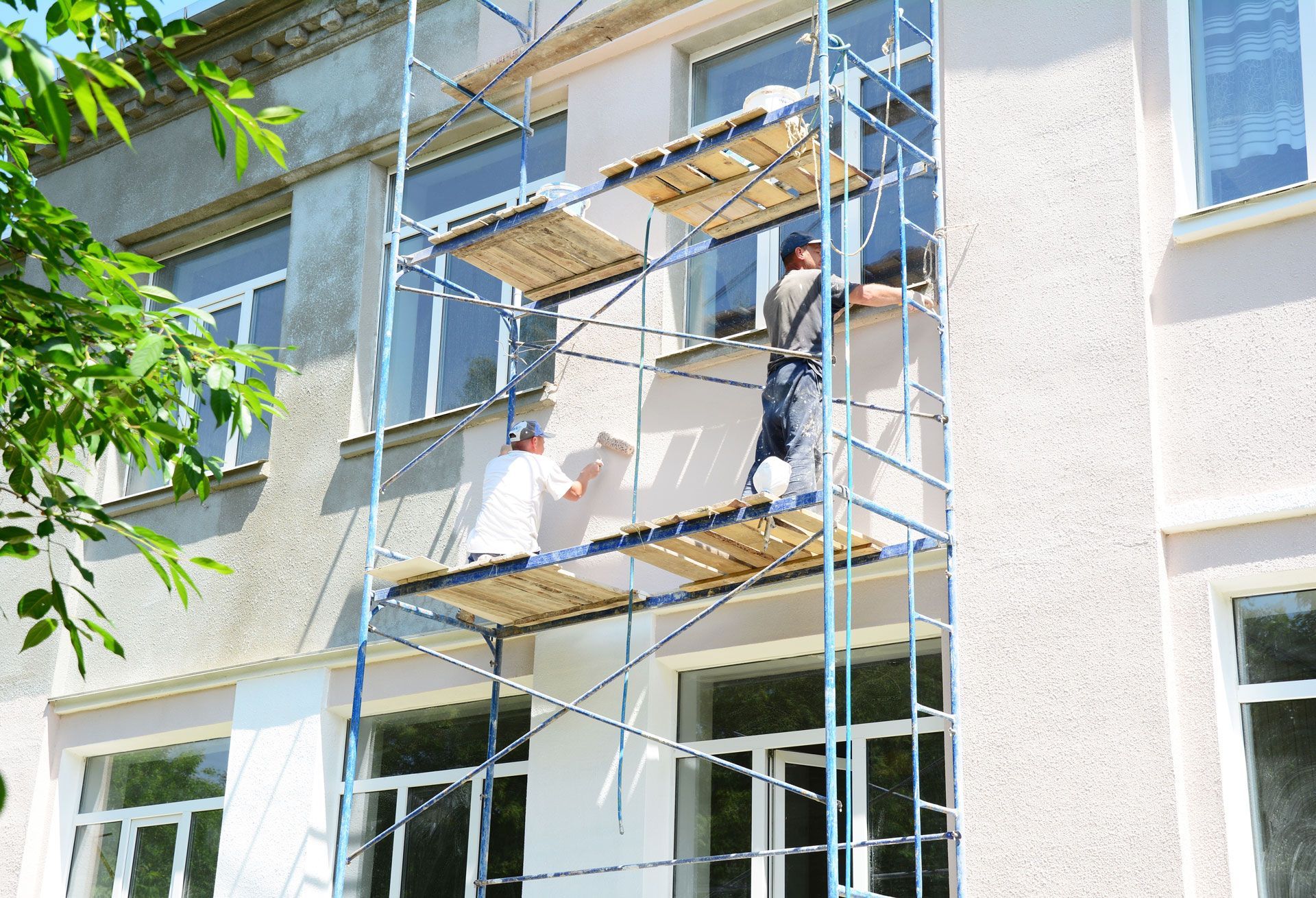 Two men are painting the side of a building on scaffolding.