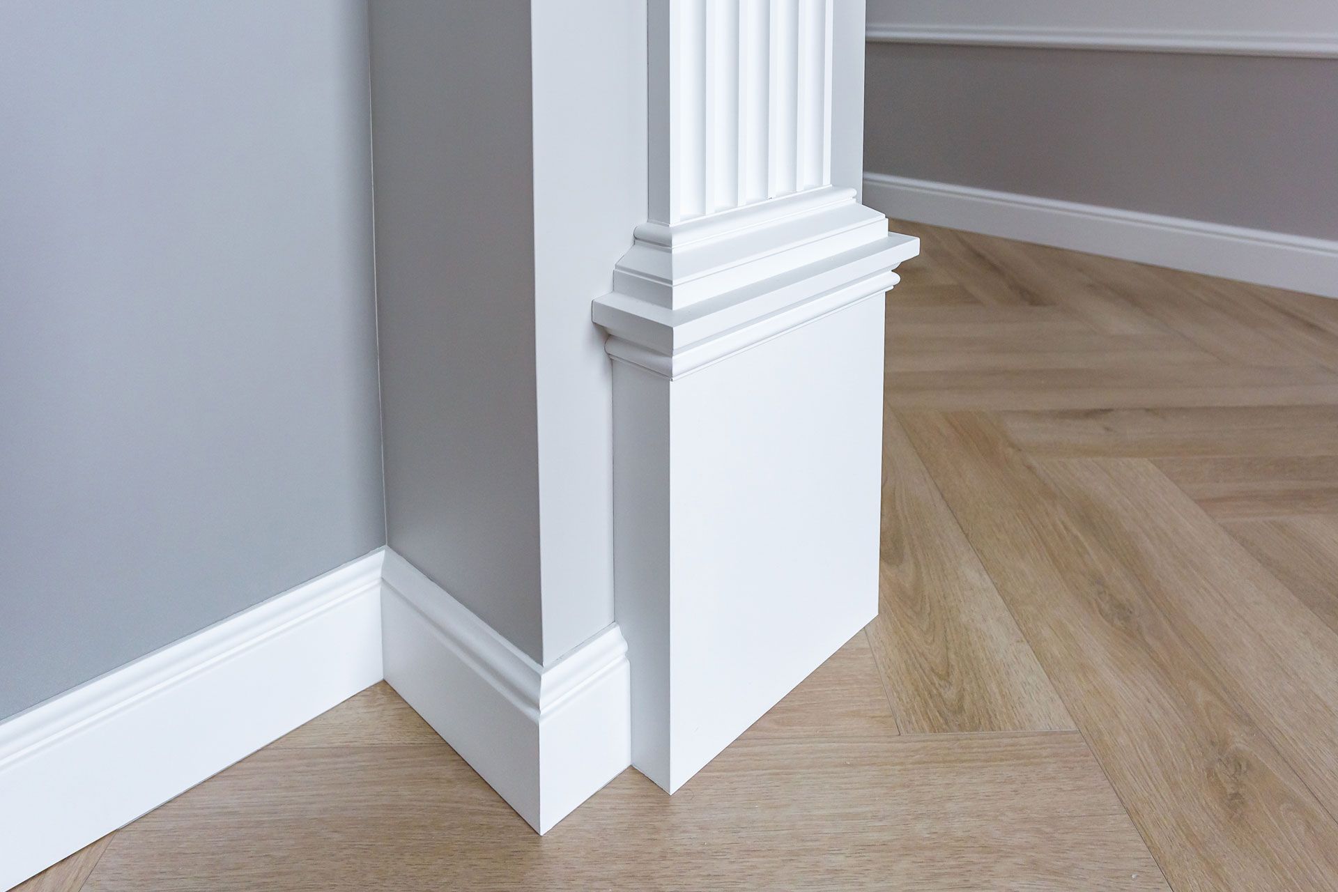 A corner of a room with white molding and a wooden floor.