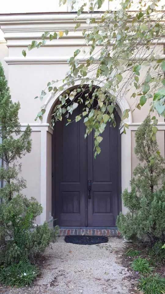 A large black door is surrounded by trees and bushes.
