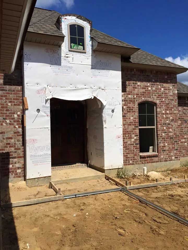 A brick house is being built with a large door and windows.