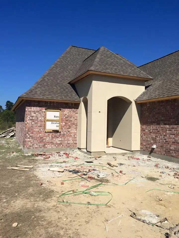 A brick house is being built in the middle of a dirt field.